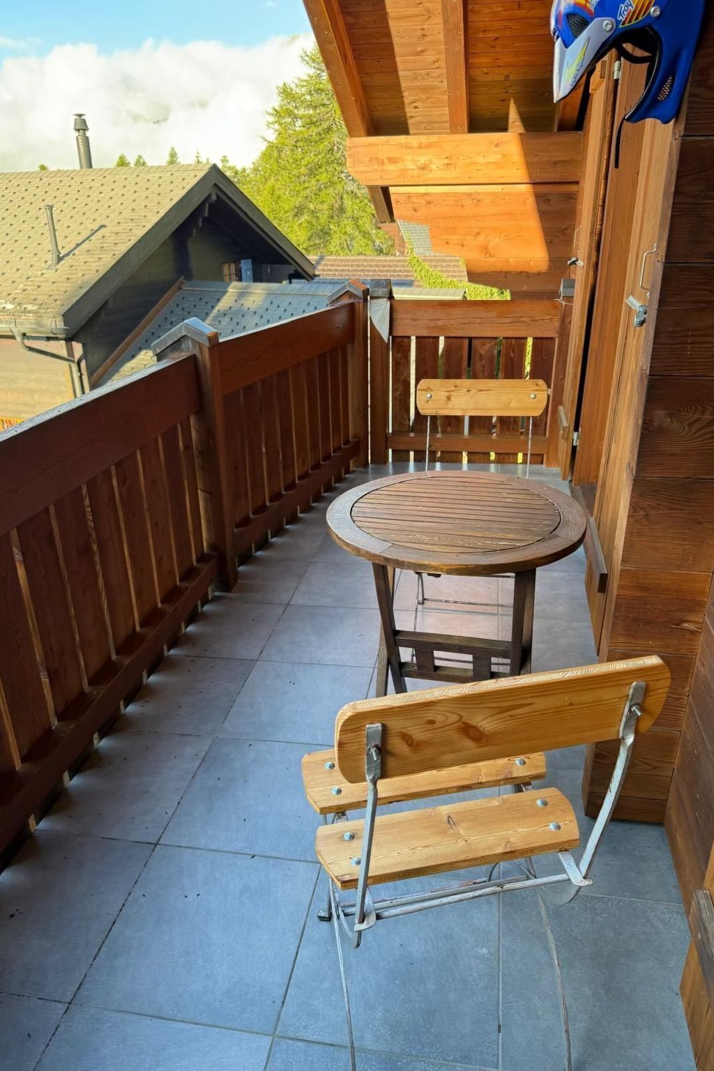 Een houten terras met een ronde tafel en twee bankjes.