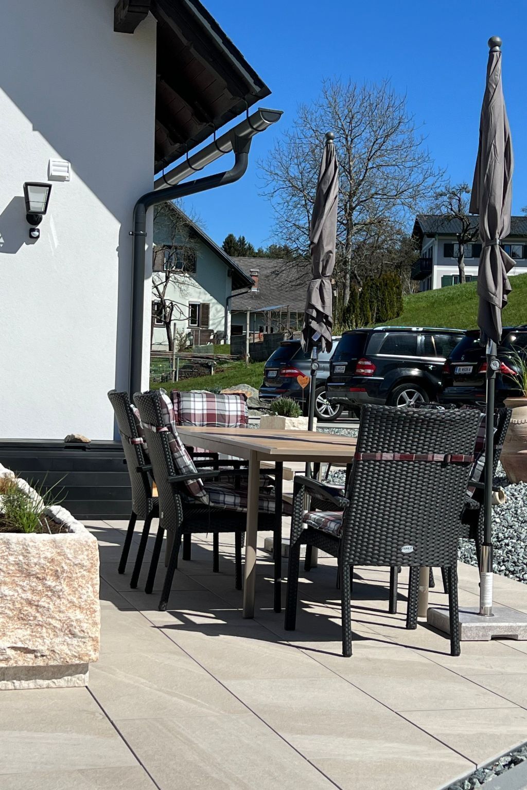 Un espacio al aire libre con patio, una mesa, sillas, sombrillas y una jardinera de piedra.