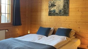 Une pièce en bois avec un lit, une fenêtre avec des rideaux, un tableau accroché au mur et un luminaire suspendu au plafond.