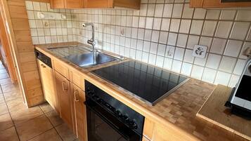 Une cuisine de taille réduite, avec des meubles en bois, une cuisinière noire, un évier et un lave-vaisselle.