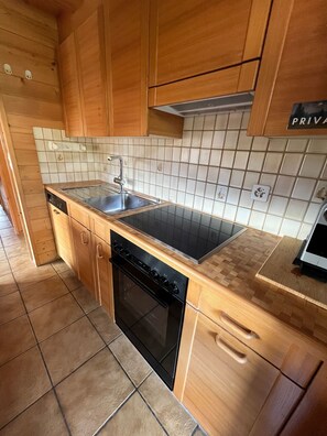 Une cuisine de taille réduite, avec des meubles en bois, une cuisinière noire, un évier et un lave-vaisselle.