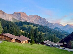 A mountain cabin with a sloped roof, surrounded by lush green hills and a backdrop of rugged mountains. - Chalet Bärgblüemli by Interhome (Frutigen)