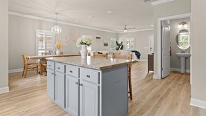 Een ruime keuken met een groot eiland, houten vloeren en een eetgedeelte met een tafel en stoelen.