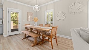 Een eethoek met een houten tafel, rieten stoelen, een kroonluchter en decoratieve wanddecoratie.