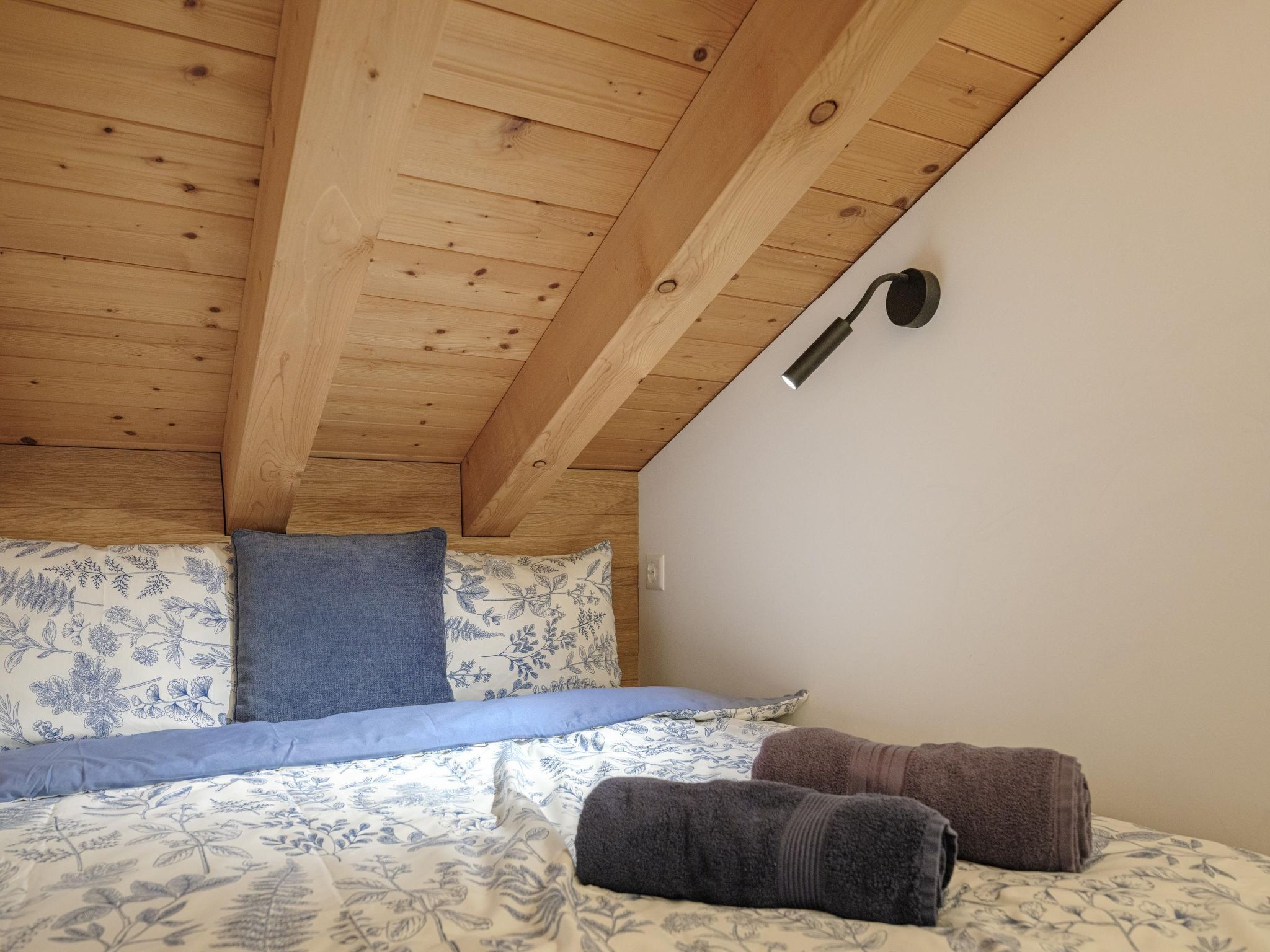 A bedroom with a wooden ceiling, a bed with floral bedding, and two rolled towels.