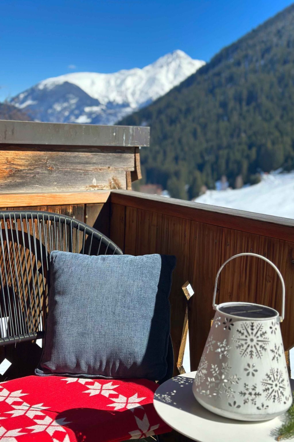 Een balkon met een houten hekwerk, een stoel, een kussen en een lantaarn.