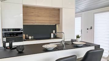 A modern kitchen with a central island, black bar stools, and a built-in oven.