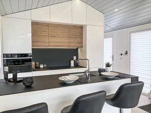Cozinha moderna com ilha central, banquetas pretas e forno embutido.