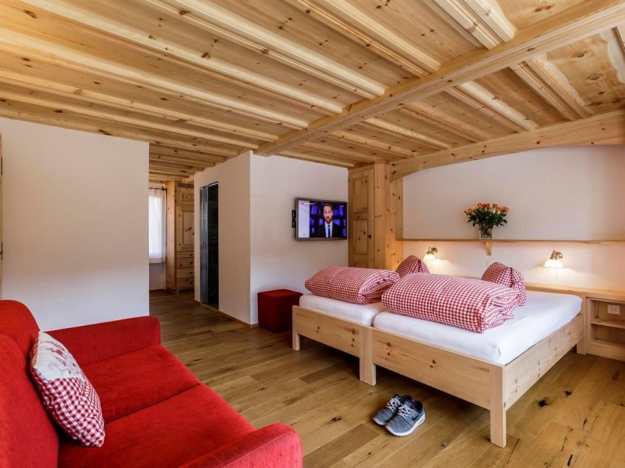 Ein Zimmer mit Holzboden, einem Bett, einem roten Sofa und einem Fernseher an der Wand.
