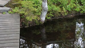 A cabin with a porch, a small deck, and a pond in front.