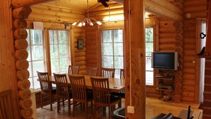 A log cabin interior with a dining area, wooden walls, and a television.