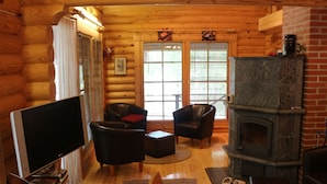A cozy log cabin interior with a fireplace, wooden walls, a television, and two leather chairs.