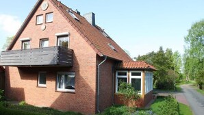 Ein zweistöckiges Backsteinhaus mit einem geneigten Dach, einem Balkon im oberen Geschoss und einem gepflegten Garten mit verschiedenen Pflanzen und Blumen.