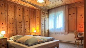 Un dormitori amb llit, taules de nit, una cadira i una finestra amb cortines.