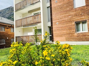 A multi-story building with balconies, a wooden facade, and a grassy area with yellow flowers. - Apartment Cervin by Interhome (Zermatt)