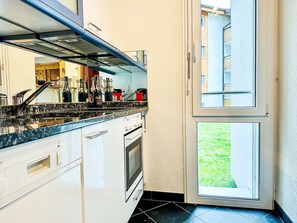 A kitchen with a built-in oven, a stainless steel sink, and a window overlooking a grassy area. - Apartment Cervin by Interhome (Zermatt)