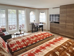 A bedroom with two beds, a desk, a chair, a TV, and large windows. - Geräumiges Studio (42 m²) – Matterhorn Panoramab by Interhome (Zermatt)