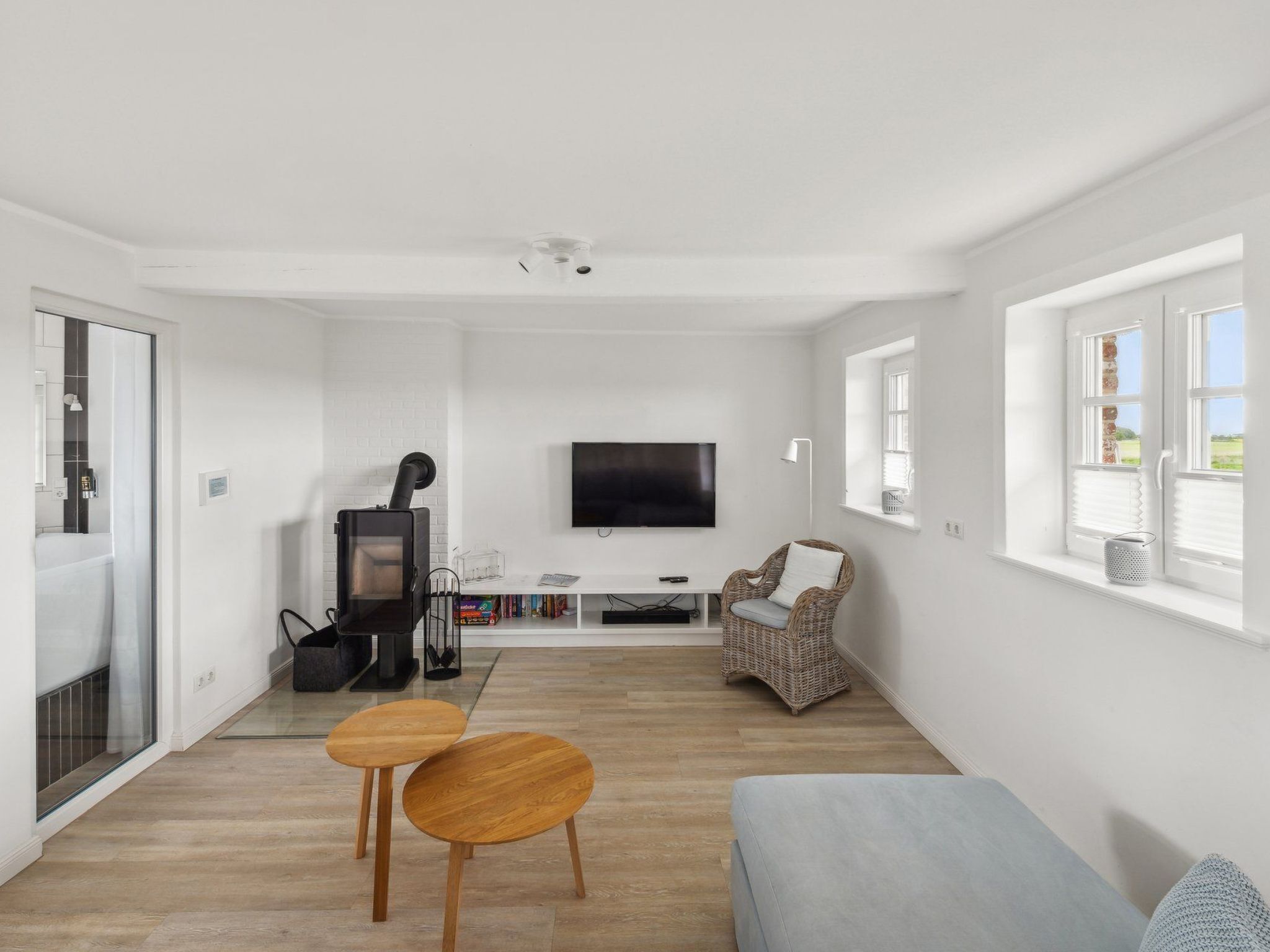 A modern living room with a fireplace, a flat-screen TV, a sofa, and a dining area with two wooden tables.