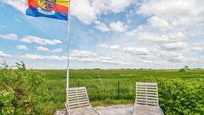 Två träloungestolar på en stenlagd uteplats, med en flaggstång och en flagga i bakgrunden.