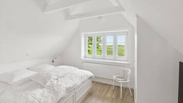 Et hvidt soveværelse med seng, et vindue med udsigt til grøn natur og en radiator.