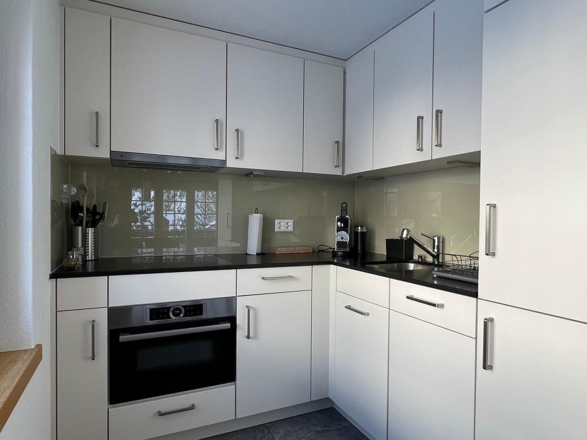 Una cucina moderna con mobili bianchi, un piano di lavoro nero, elettrodomestici in acciaio inossidabile e una finestra vista alberi.