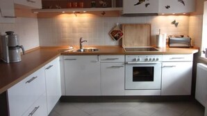 Een kleine keuken met witte kastjes, een inbouwoven, een spoelbak en een broodrooster.