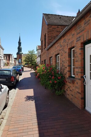 A brick building with a white door, a paved sidewalk, and parked cars. - Apartment Reindl by Interhome (Tönning)