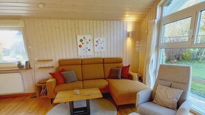 Ein gemütliches Wohnzimmer mit Holzboden, einer Couch, einem Sessel und einem Couchtisch. Darüber befinden sich zwei Wandbilder.