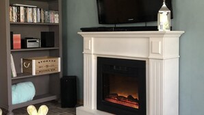 Ein Wohnzimmer mit Kamin, einem darüber montierten Fernseher und einer Bücherwand voller Bücher.