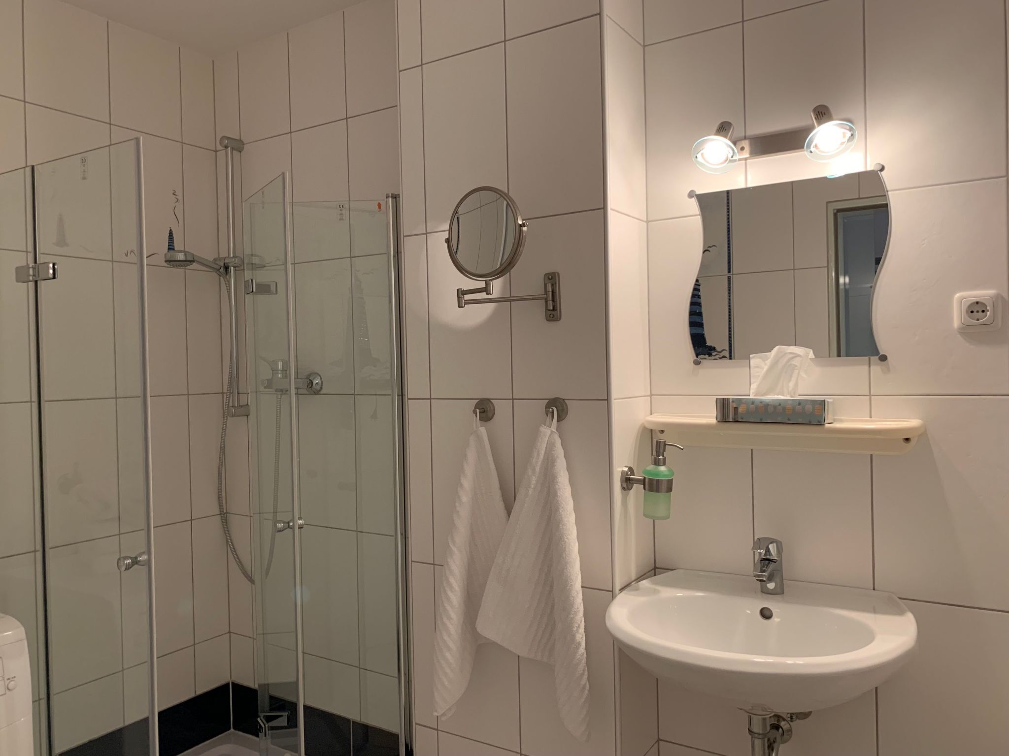 Ein modernes Badezimmer mit einer Duschkabine aus Glas, einem weißen Waschbecken und einem Spiegel mit Beleuchtung darüber.