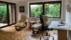 Een ruime kamer met een groot raam, een bureau, twee stoelen en een klein tafeltje.