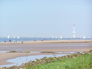 A beach with a lighthouse, sandy shore, and sailboats in the distance. - Elbe-Ferienwohnung mit Terrasse nah am Zentrum by Interhome (Glückstadt)