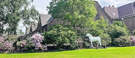 A grassy lawn with a white horse statue, surrounded by trees and shrubs, with a building in the background.