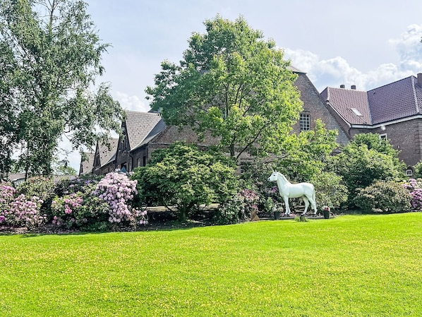 A grassy lawn with a white horse statue, surrounded by trees and shrubs, with a building in the background.