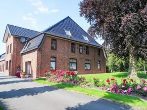 A two-story brick building with a sloped roof, large windows, and a well-maintained garden with flowers. - Studio Appartement Gartenblick by Interhome (Elskop)