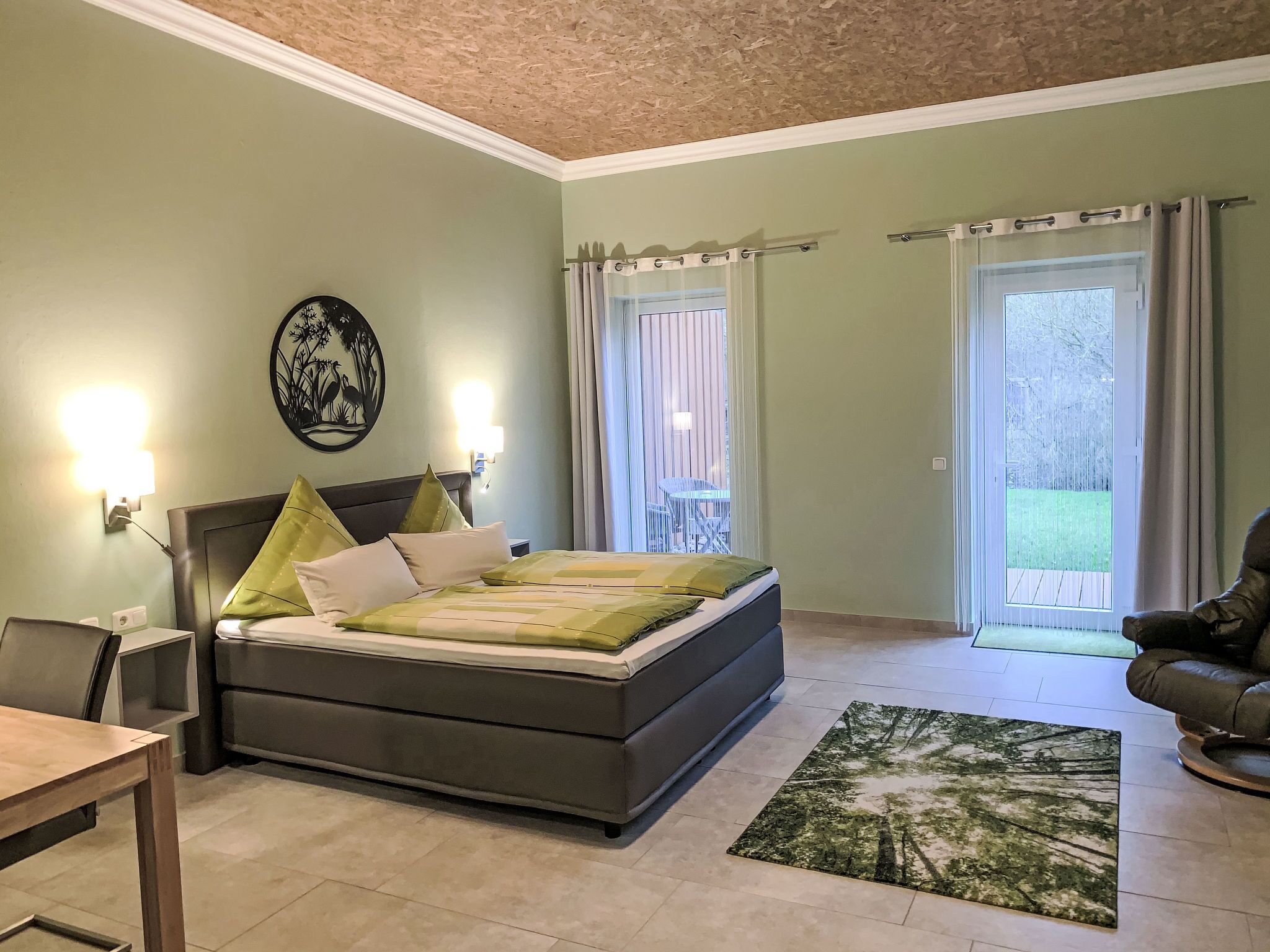 Ein Schlafzimmer mit Bett, Stuhl, Tisch und Blick ins Freie.