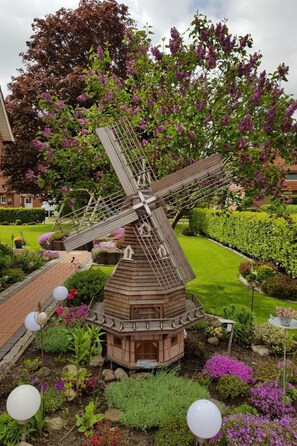 A windmill in a garden with a brick base, surrounded by various plants and flowers. - Beim Bracksee by Interhome (Wischhafen)
