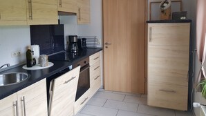 Una cucina compatta con mobili in legno, un piano di lavoro nero, una macchina da caffè e un frigorifero.