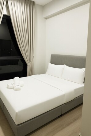 Ein modernes Hotelzimmer mit einem großen Bett, grauem Kopfteil, weißer Bettwäsche und Blick auf die Stadt bei Nacht.