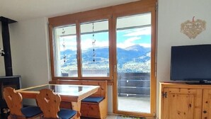 Ein Essbereich mit Holztisch und -stühlen, einem Fernseher auf einer Holzkommode und Blick auf Berge durch große Fenster.