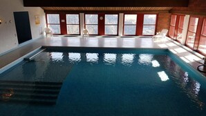 Ein Hallenbad mit klaren Fenstern, Stufen zum Pool und weißen Liegestühlen.
