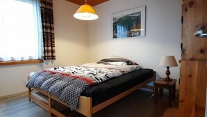 Ein Schlafzimmer mit Holzwänden, einem Bett, einer Hängelampe, einem Gemälde und einem Fenster mit Vorhängen.