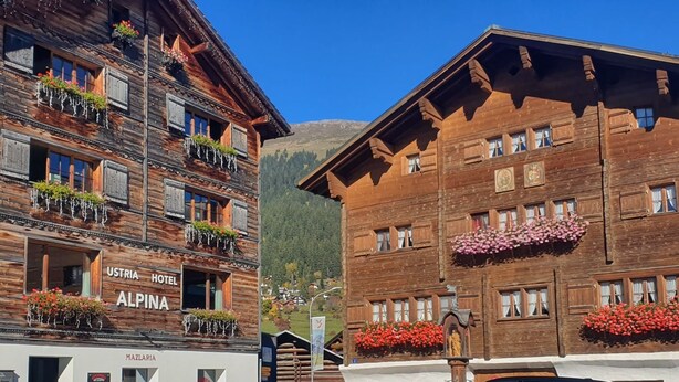 Ein traditionelles Holzgebäude mit Balkonen, die mit Blumen geschmückt sind, mit der Aufschrift "Ustria Hotel Alpena".