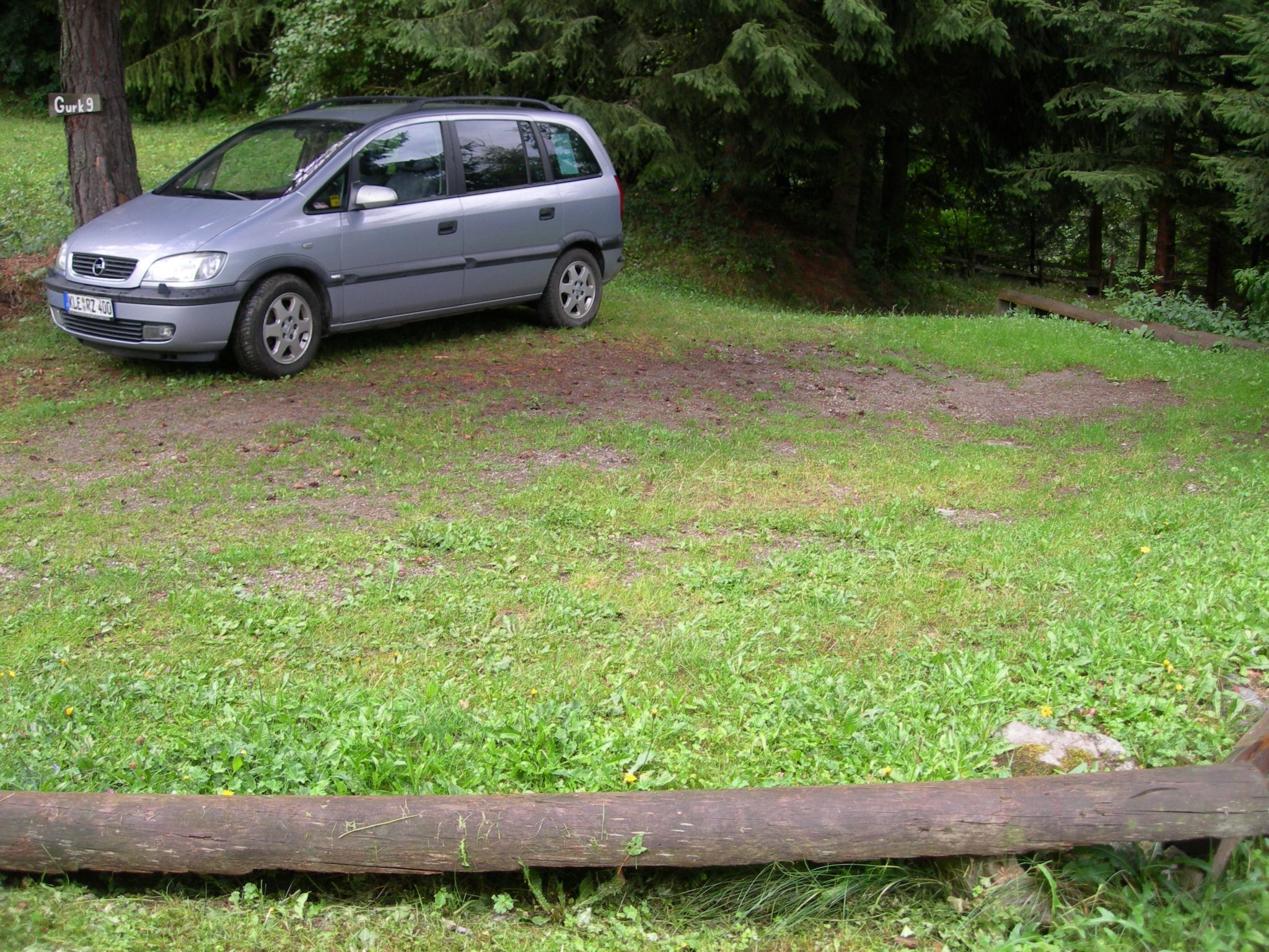Une voiture argentée est garée sur une pelouse, avec une clôture en bois en premier plan.