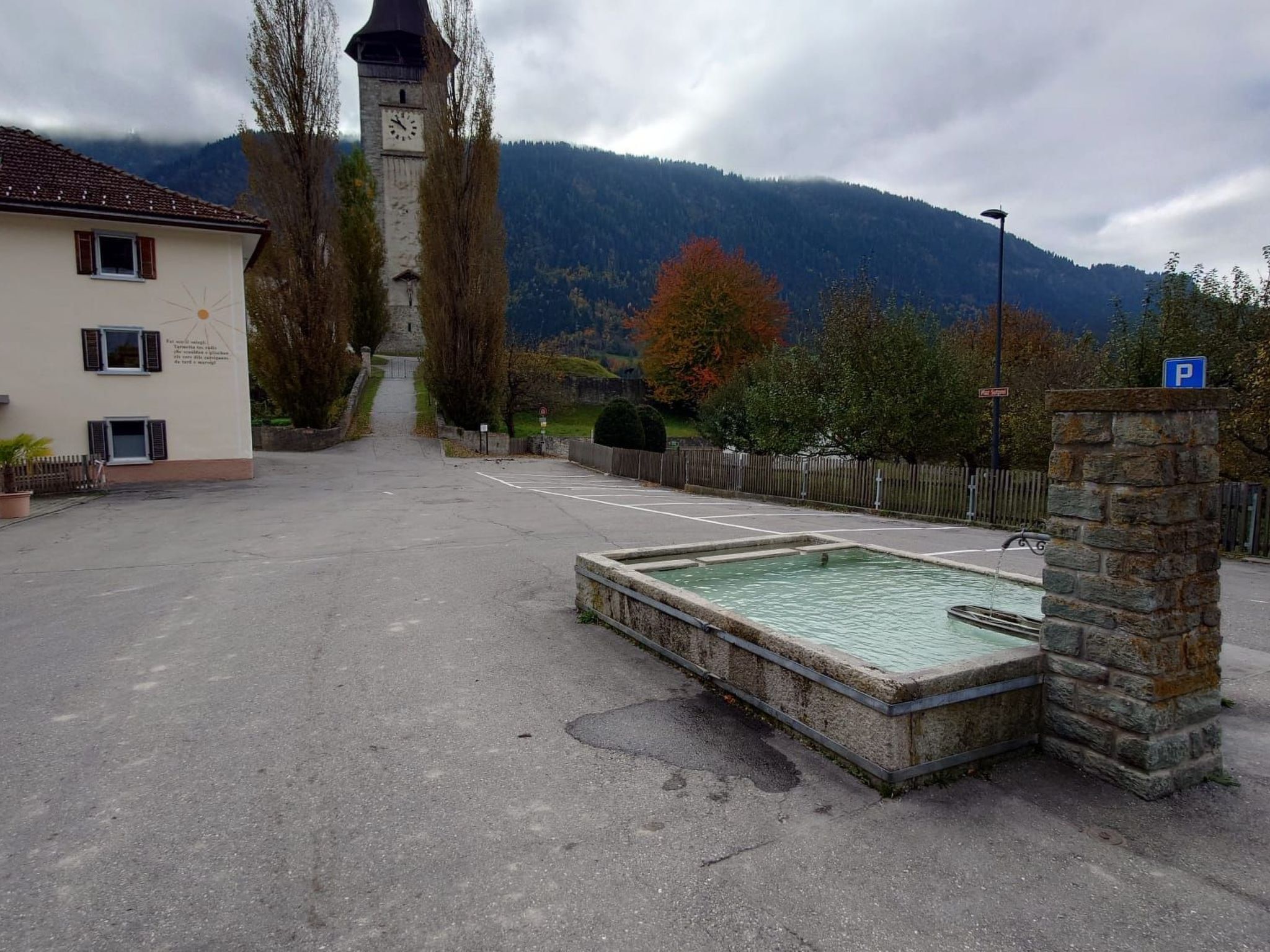 Ein Parkplatz mit einem Steinfbrunnen, einem Glockenturm und einem Gebäude mit einem Schild.