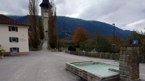 A parking area with a stone fountain, a clock tower, and a building with a sign. - Apartment Günter by Interhome (Sagogn)