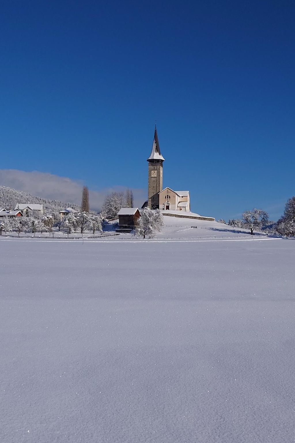 Schneebedeckte Landschaft mit einer Kirche, die einen hohen Turm und eine Uhr zeigt.