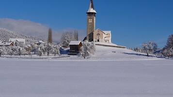 Schneebedeckte Landschaft mit einer Kirche, die einen hohen Turm und eine Uhr zeigt.