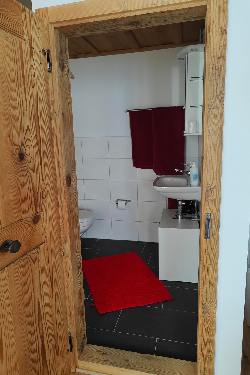 A wooden-framed bathroom with a white sink, red towels, and a red rug on the floor.