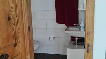A wooden-framed bathroom with a white sink, red towels, and a red rug on the floor.